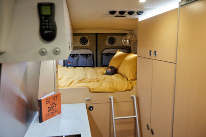 Compact living space with a bed, cabinets, and a ladder inside a vehicle