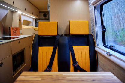 Interior of a vehicle with yellow and black seats and a window showing greenery outside.