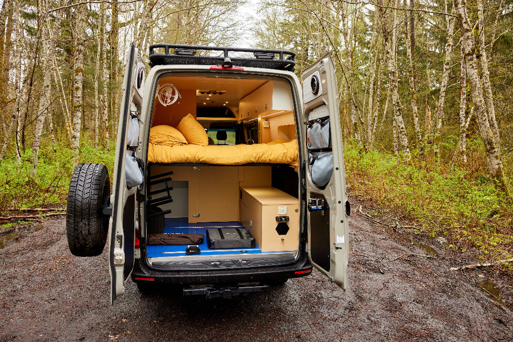 Van conversion with sleeping area and storage in a forest setting