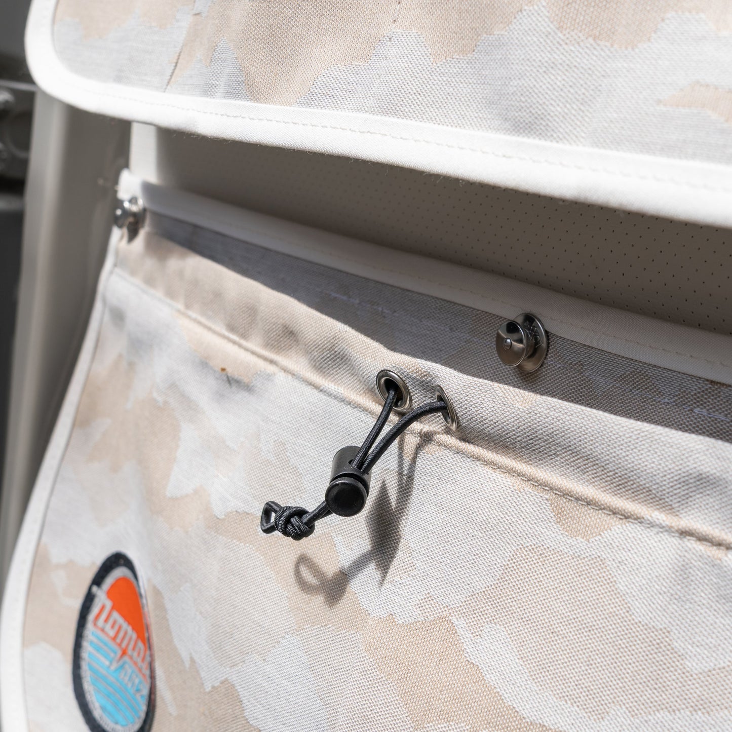 Macro detail of the Nomad Vanz Rear Door Storage Pocket System in Cirrus Sand camo showing the bungee drawstring cord closure, snap fastener, white piping trim, and Nomad Vanz logo patch on durable canvas fabric