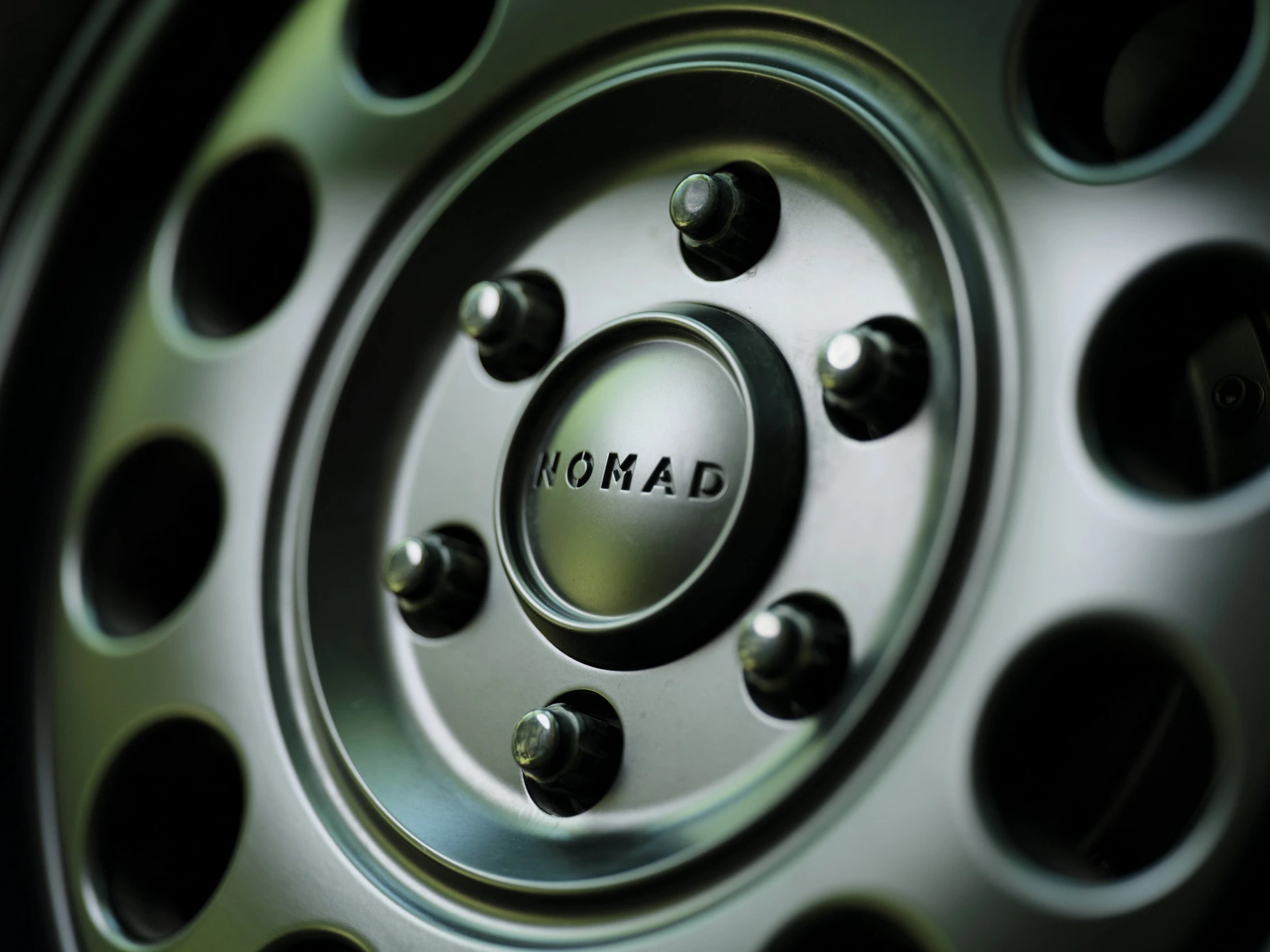 Macro detail of the Nomad-branded center cap and lug nuts on the wheel of a Nomad Vanz Hygge Sprinter camper van