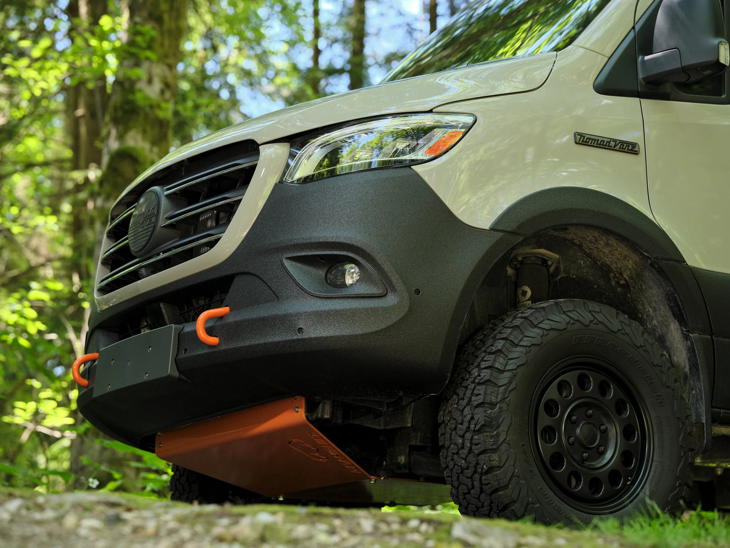 Close-up of a Nomad Vanz Sprinter 4x4 front corner showing BFGoodrich all-terrain tire, black off-road wheel, and front skid plate