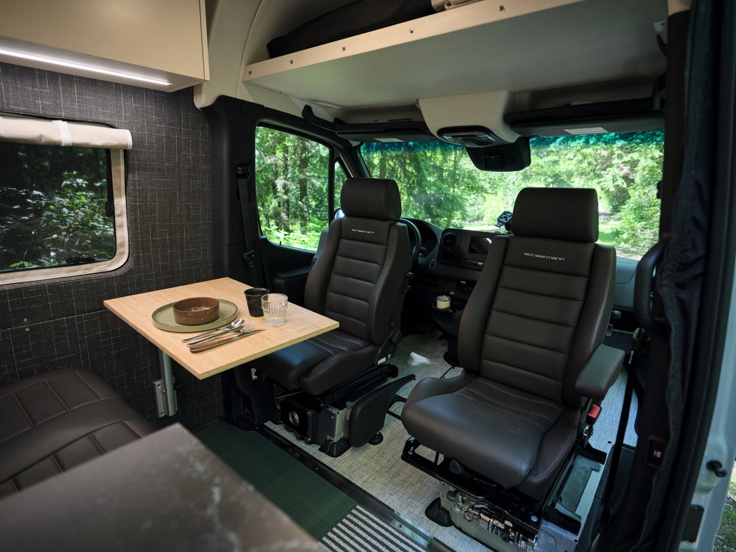 Interior of a Nomad Vanz Sprinter showing a bamboo dinette table set for a meal with Scheel-Mann leather swivel cab seats