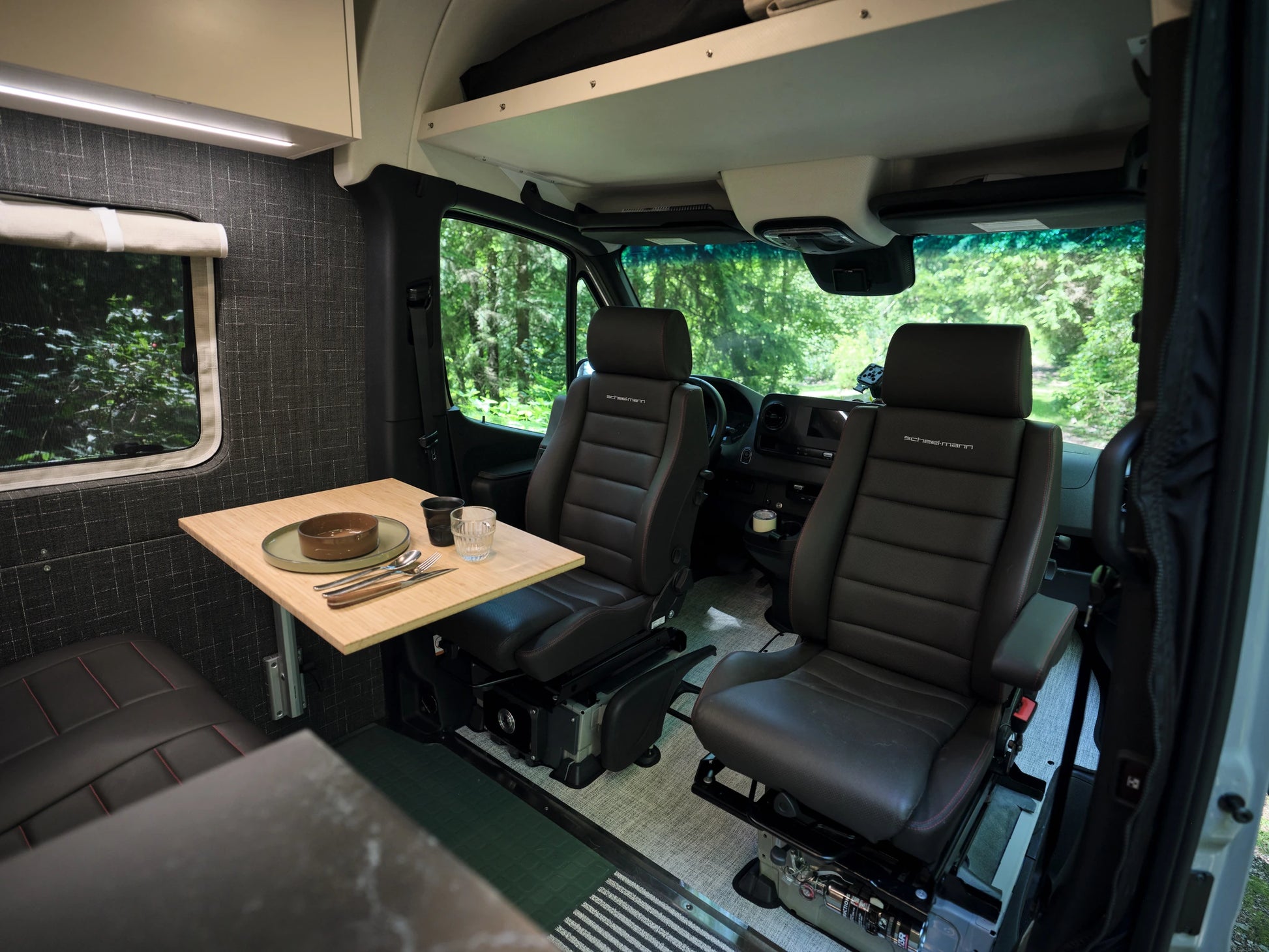 Interior of a Nomad Vanz Sprinter showing a bamboo dinette table set for a meal with Scheel-Mann leather swivel cab seats