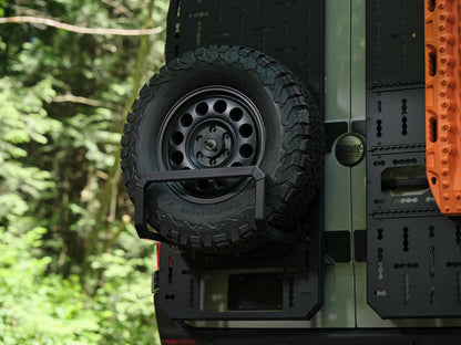 Rear door of a Nomad Vanz Sprinter with swing-out spare tire carrier, storage panel, and orange traction boards