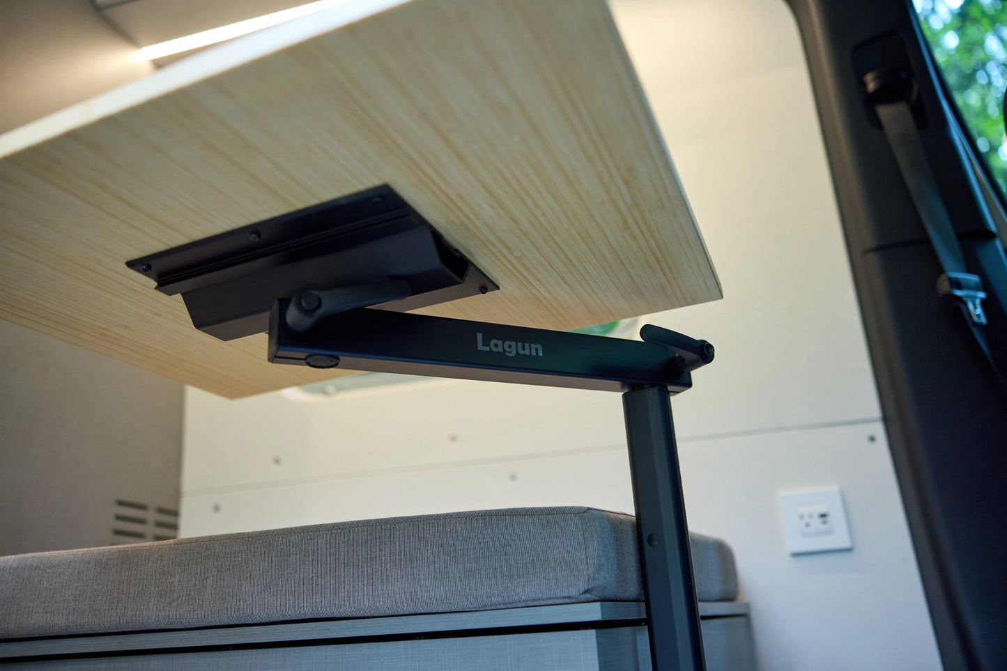 Underside detail of a Lagun swivel table mount and bamboo tabletop above a gray bench seat inside a Nomad Vanz Twoonie Sprinter camper van